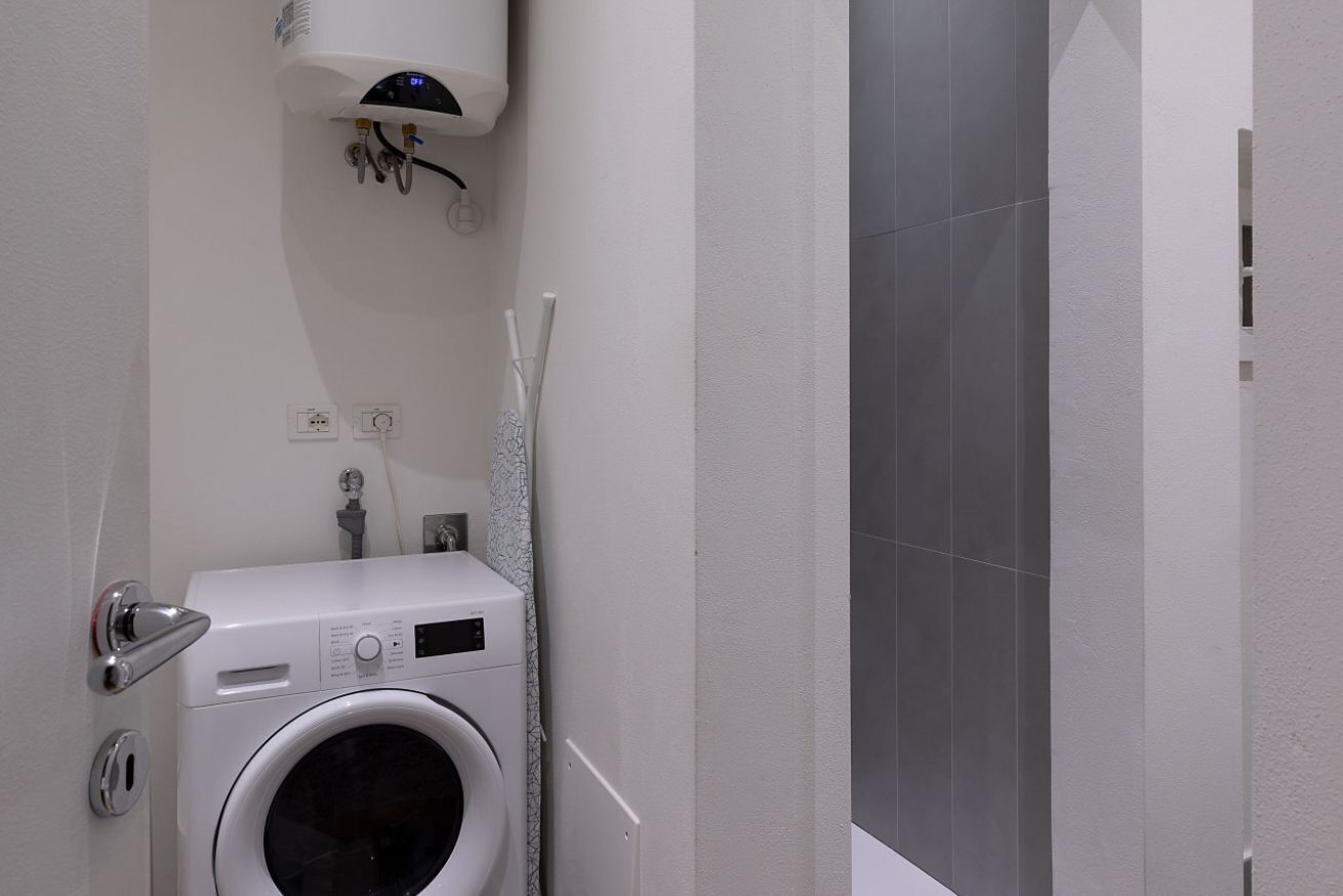 Ein kleiner Waschbereich mit einer Frontlader-Waschmaschine, einem Wandheizkörper und einer Duschkabine.