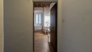 Een smalle gang die uitkomt in een eetruimte, met een houten vloer, witte muren en een raam met uitzicht.