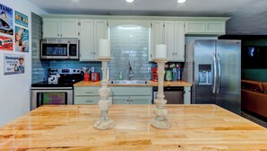 A kitchen with light green cabinets, a stainless steel refrigerator, a microwave, and a wooden island with two candle holders.
