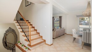 Un vaste espace de vie agrémenté d’un escalier en bois, un coin repas avec une nappe à rayures et une vue dégagée sur l’extérieur grâce à une porte vitrée.
