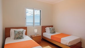 Une chambre avec deux lits, une table de chevet et une fenêtre donnant sur la mer.