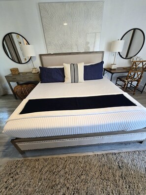 A neatly made bed with a headboard, two bedside tables with lamps, a chair, and a textured wall art piece.
