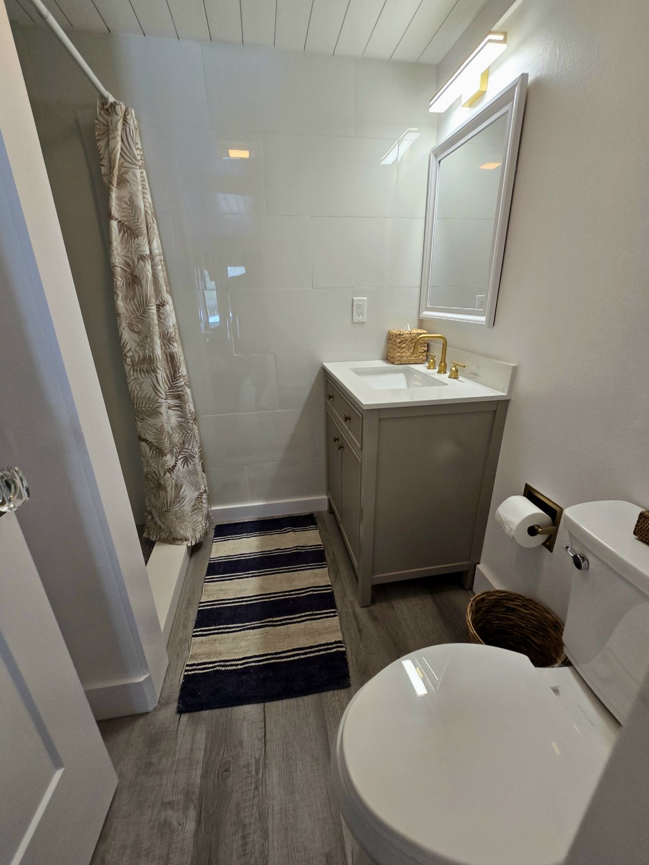 A bathroom with a shower, toilet, sink, and a mirror.