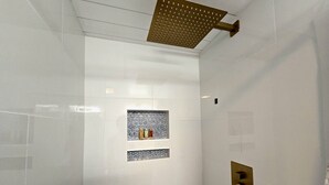 Un bagno moderno con box doccia in vetro, mensola a incasso con oggetti decorativi e pannello comandi dorato.