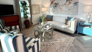 Un soggiorno moderno con un divano, poltrone a righe, un tavolino da caffè in vetro e un grande quadro astratto appeso alla parete.