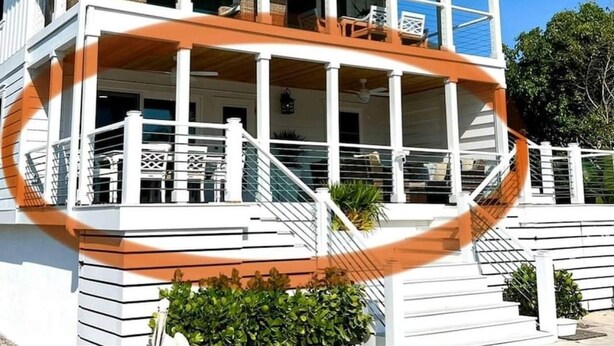 Una casa a due piani con un balcone, facciata bianca e un patio in legno.