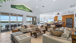 Ein großzügiger Wohnbereich mit einer großen Couch, Hocker und Couchtisch, eine Küche mit Holzausstattung und ein Balkon mit Blick aufs Wasser.