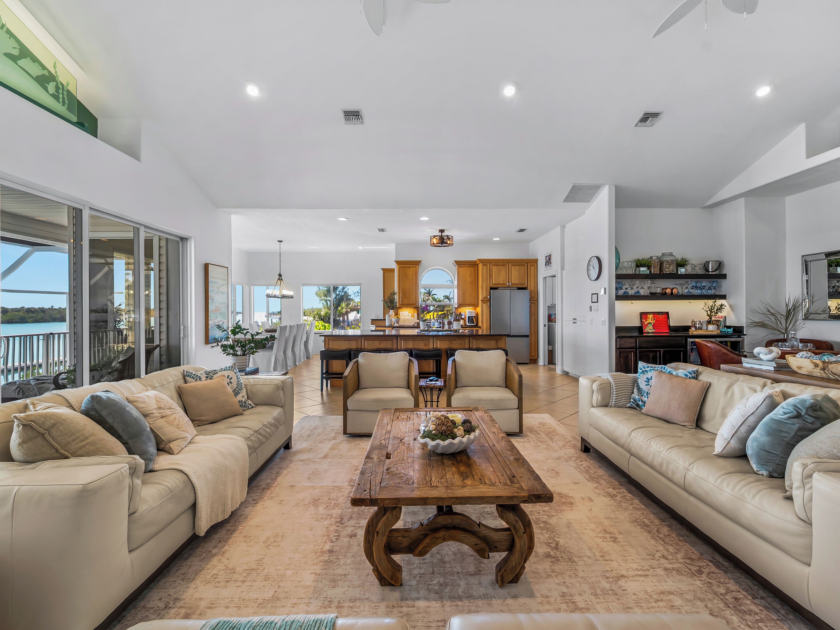 A spacious living area with a large wooden coffee table, two beige sofas, and a kitchen in the background.