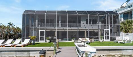 Un edificio moderno con fachada de vidrio, una terraza de madera que lleva a una piscina y asientos exteriores.