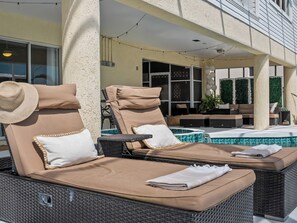 A poolside area with lounge chairs and a small table, a pool, and a covered seating area with cushions and a hat. - Bayfront home - Dock and Pool 3/3 (Englewood)