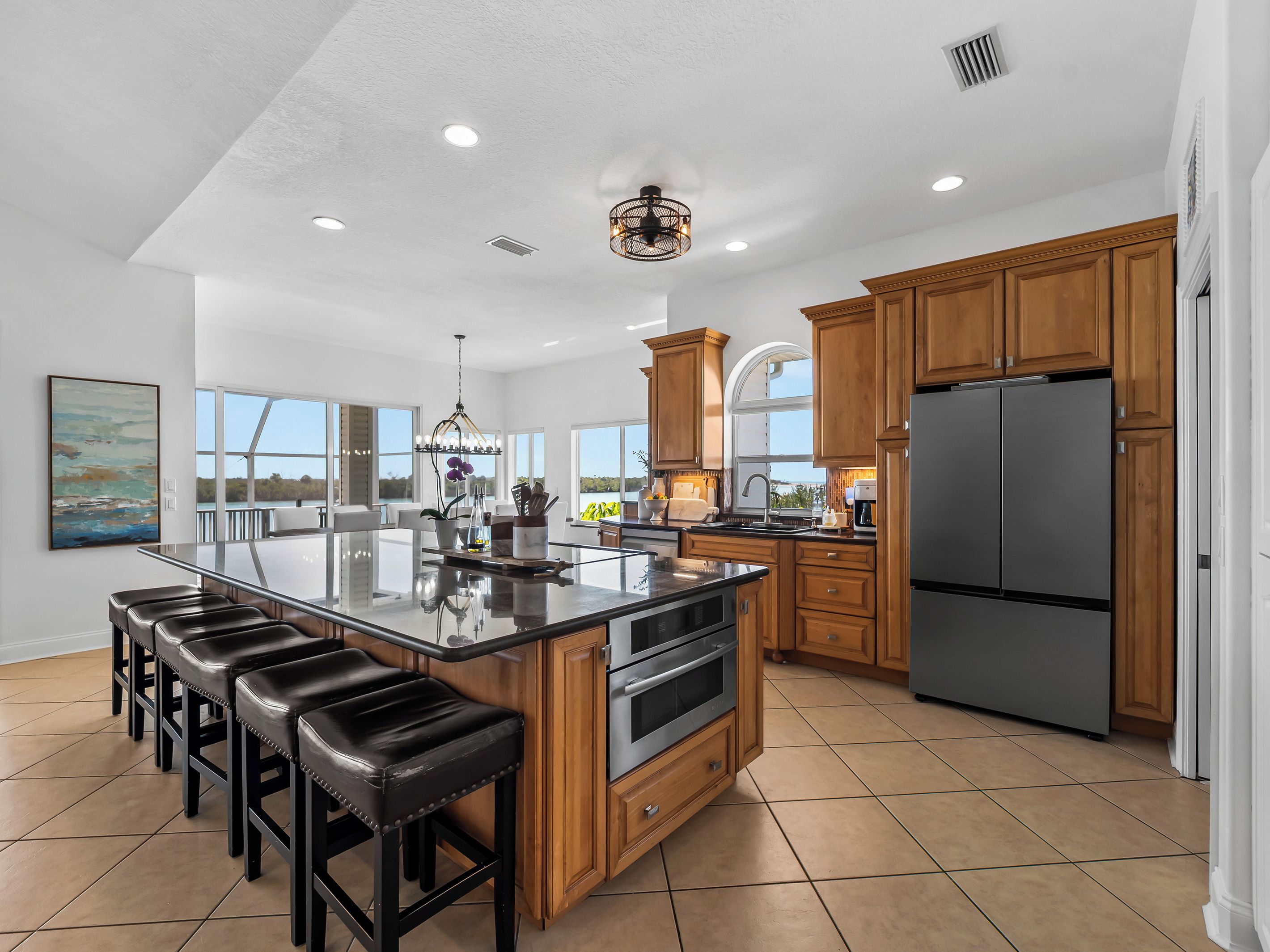 A spacious kitchen with a large island, wooden cabinets, and a stainless steel refrigerator.