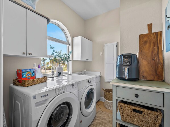 Un espace buanderie comprenant un lave-linge et un sèche-linge Whirlpool à chargement frontal, un évier et une machine à café, le tout placé sur une étagère en bois.