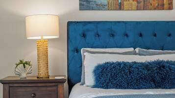 A bedroom with a tufted headboard, a bedside lamp, a nightstand, and a painting of a cityscape.