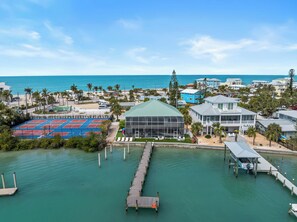 A coastal property with a tennis court, a large glass building, and a dock extending into turquoise waters. - Bayfront home - Dock and Pool 3/3 (Englewood)