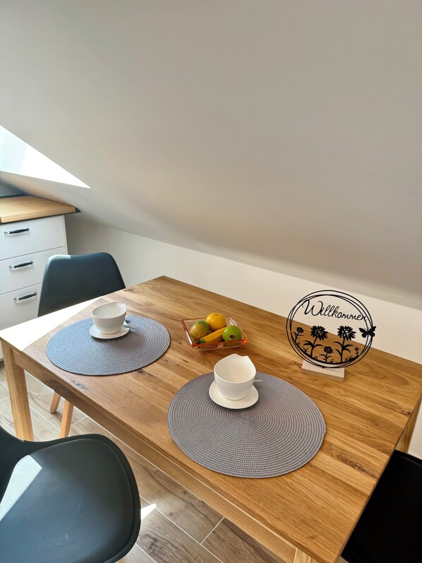 A dining table with two white bowls, a fruit bowl, and a 'Willkommen' sign.