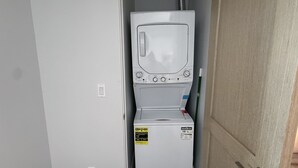 Une petite buanderie équipée d’un lave-linge et d’un sèche-linge, d’une poignée de porte et d’une prise électrique visible.