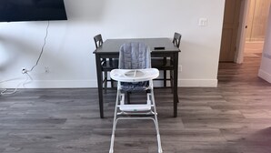 Un coin repas avec une table haute, deux chaises, une chaise haute pour bébé et un téléviseur à écran plat fixé au mur.
