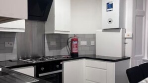Una cocina compacta con armarios blancos, una encimera negra, una estufa y un refrigerador.