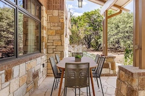An outdoor patio with stone walls, a wooden table, and wicker chairs.