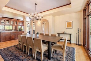 A spacious dining area with a large wooden table and six chairs, a chandelier, and a view of the kitchen with wooden cabinets.