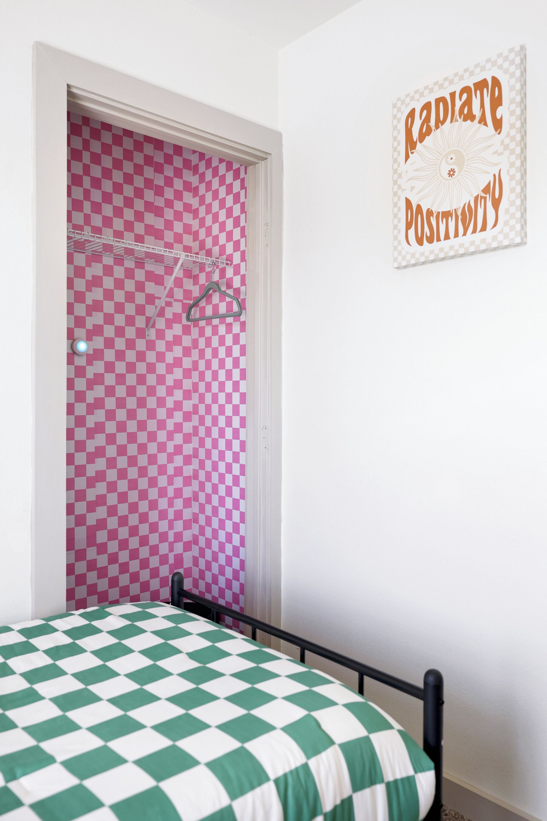 A bedroom with a checkered bedspread, a pink and white checkered door, and a motivational poster on the wall.