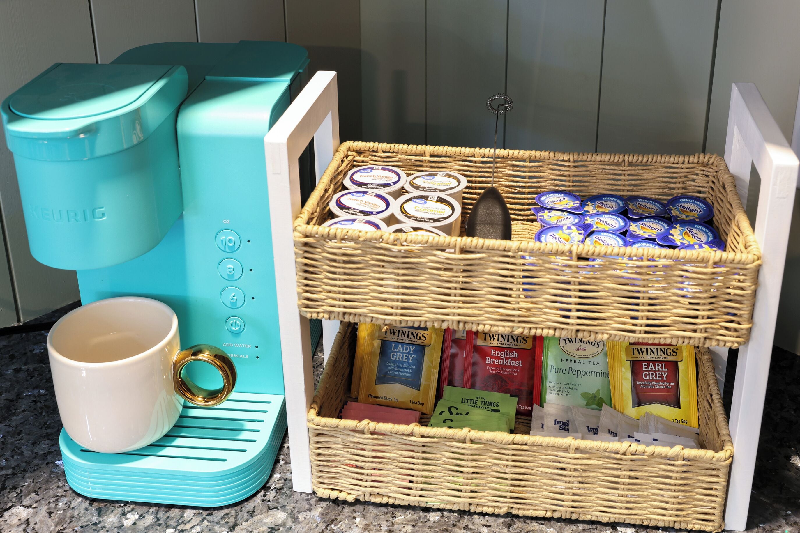 A kitchen with a teal coffee maker, a white mug, and a wicker basket containing tea bags and coffee pods.