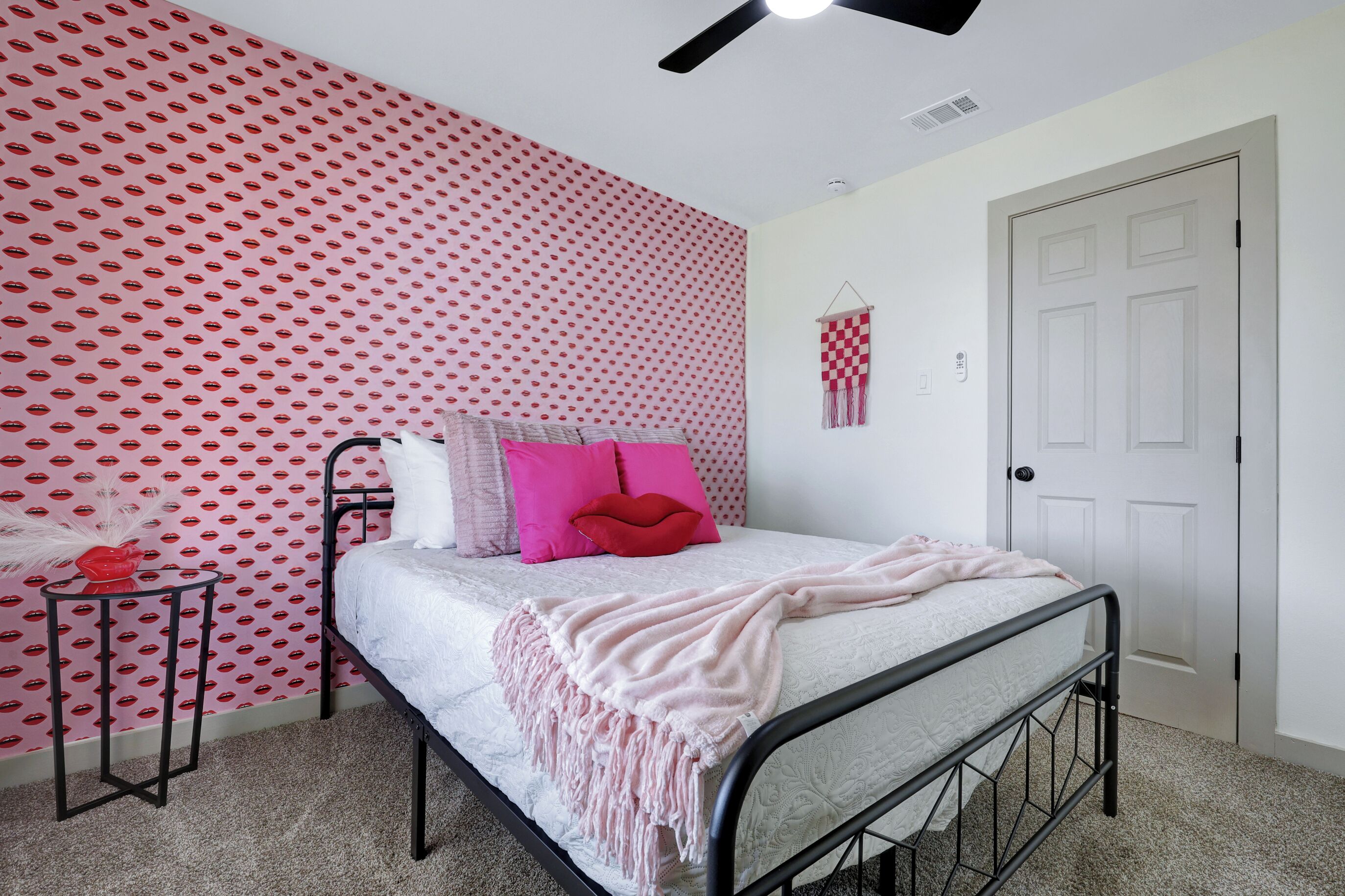 Quarto com cama, uma pequena mesa de cabeceira, parede com padrão vermelho e uma porta.