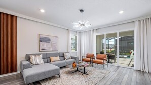 Una sala moderna con un sofá seccional gris, una mesa de centro y una puerta de cristal que da a un patio exterior.