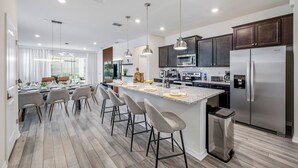 Una cocina moderna con una isla central, taburetes de bar, electrodomésticos de acero inoxidable e iluminación colgante.