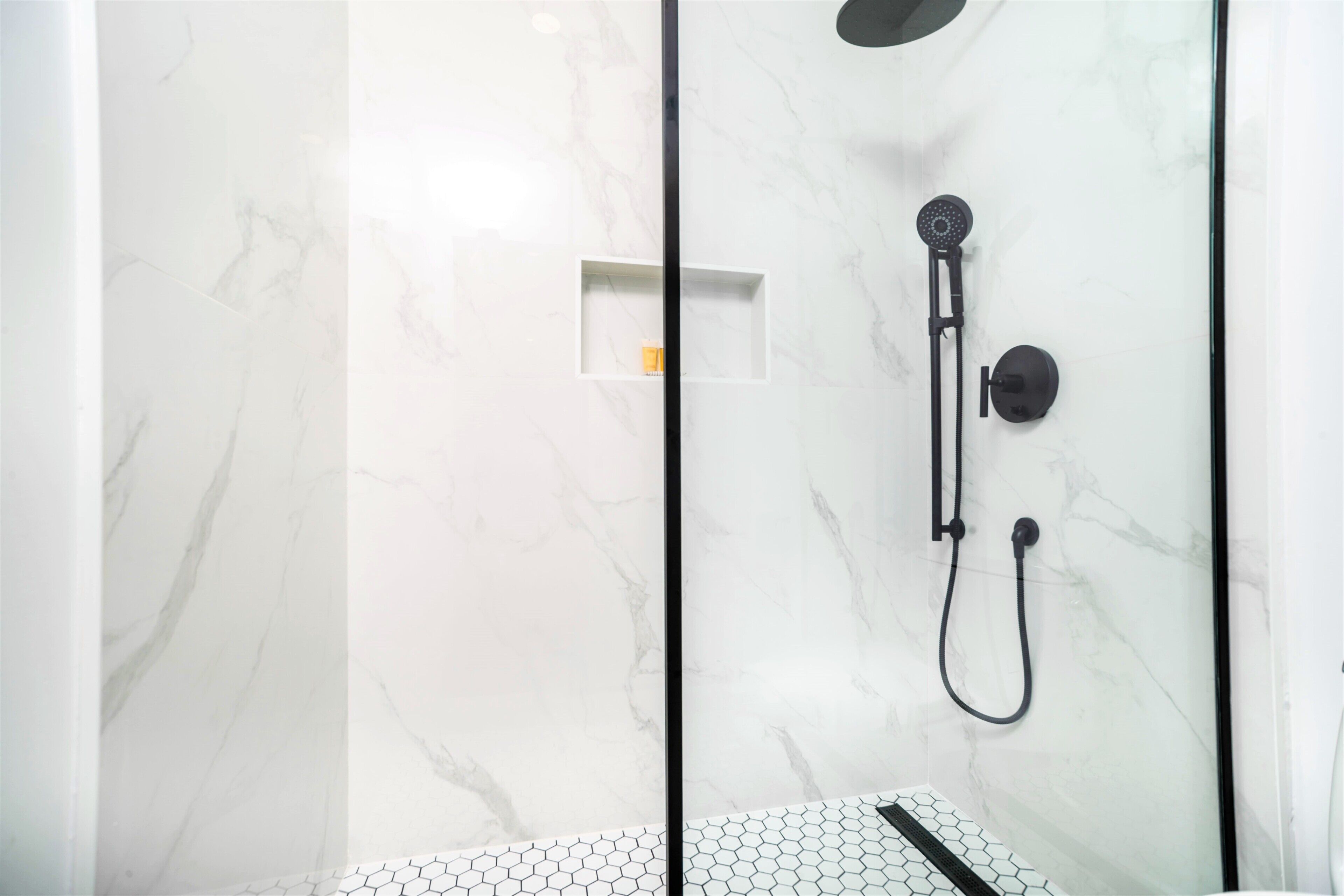 Una ducha moderna con cabina de vidrio, un cabezal de ducha de mano y mandos empotrados.