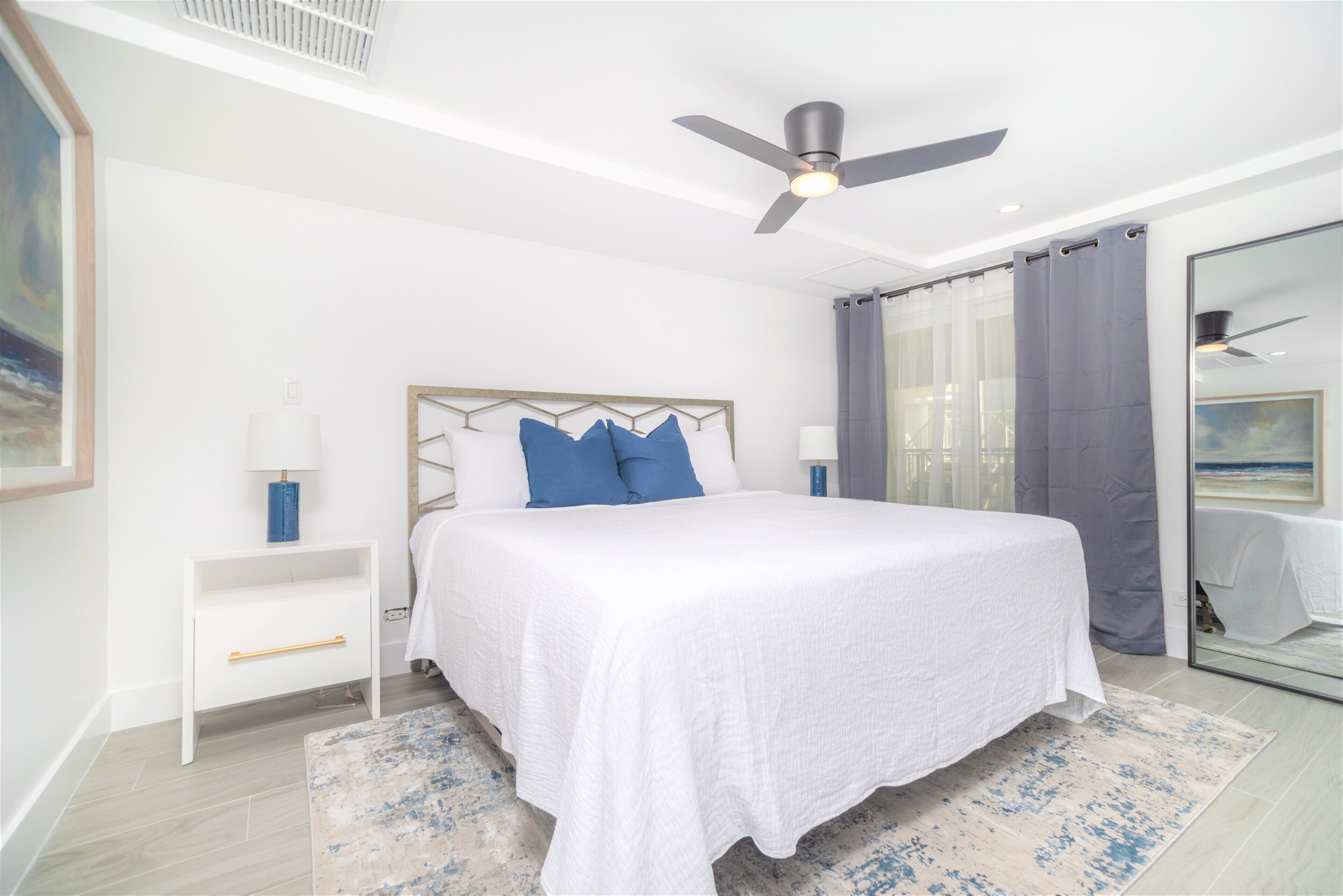 A bedroom with a bed, a nightstand, a ceiling fan, and a large window with curtains.