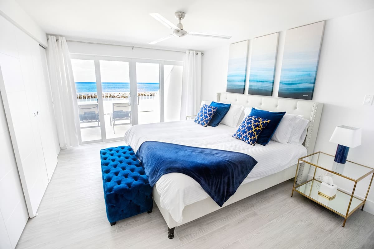 Un dormitorio con una cama grande, una mesita de vidrio y vista a la playa.