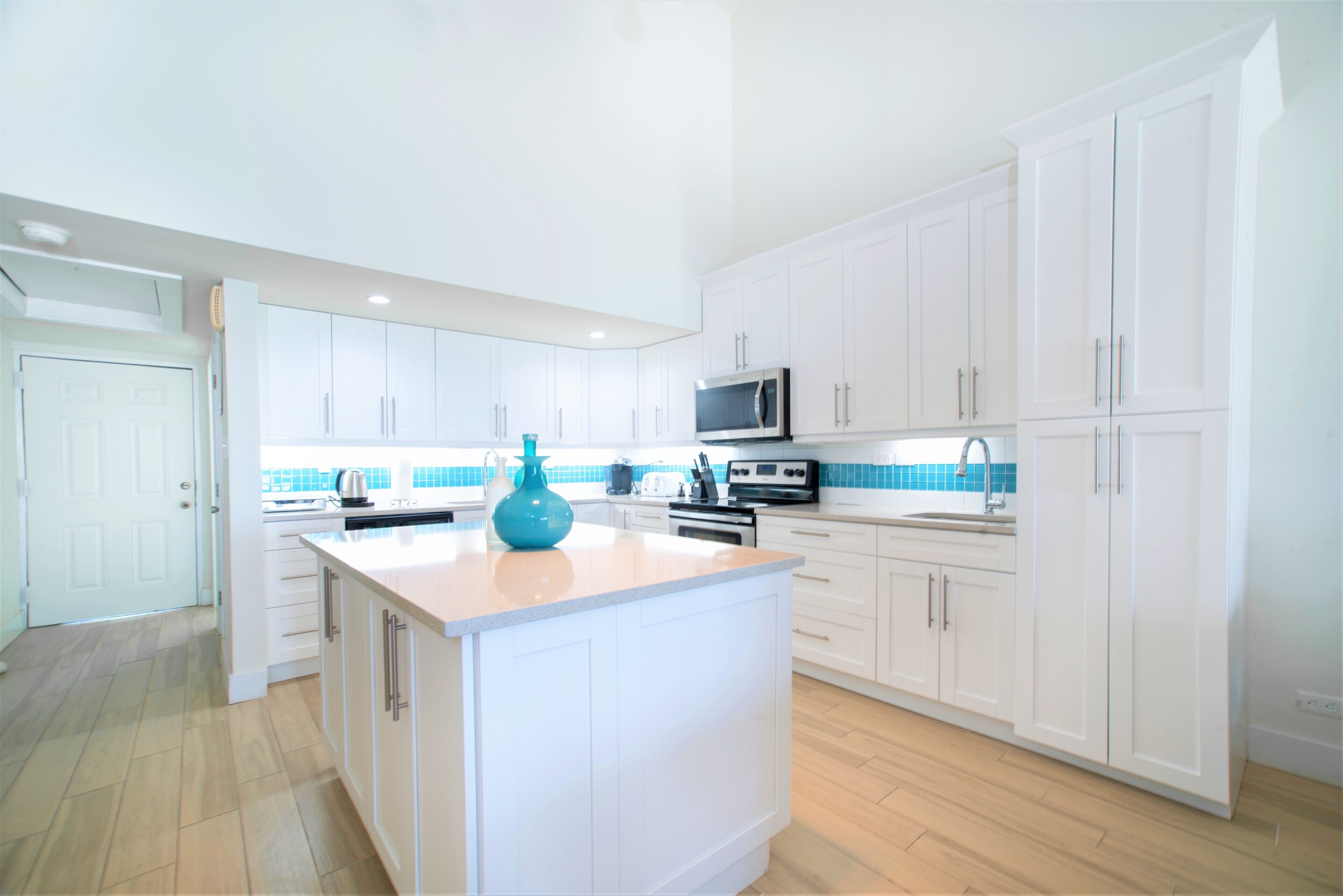 A modern kitchen with white cabinets, a central island, and a blue backsplash.