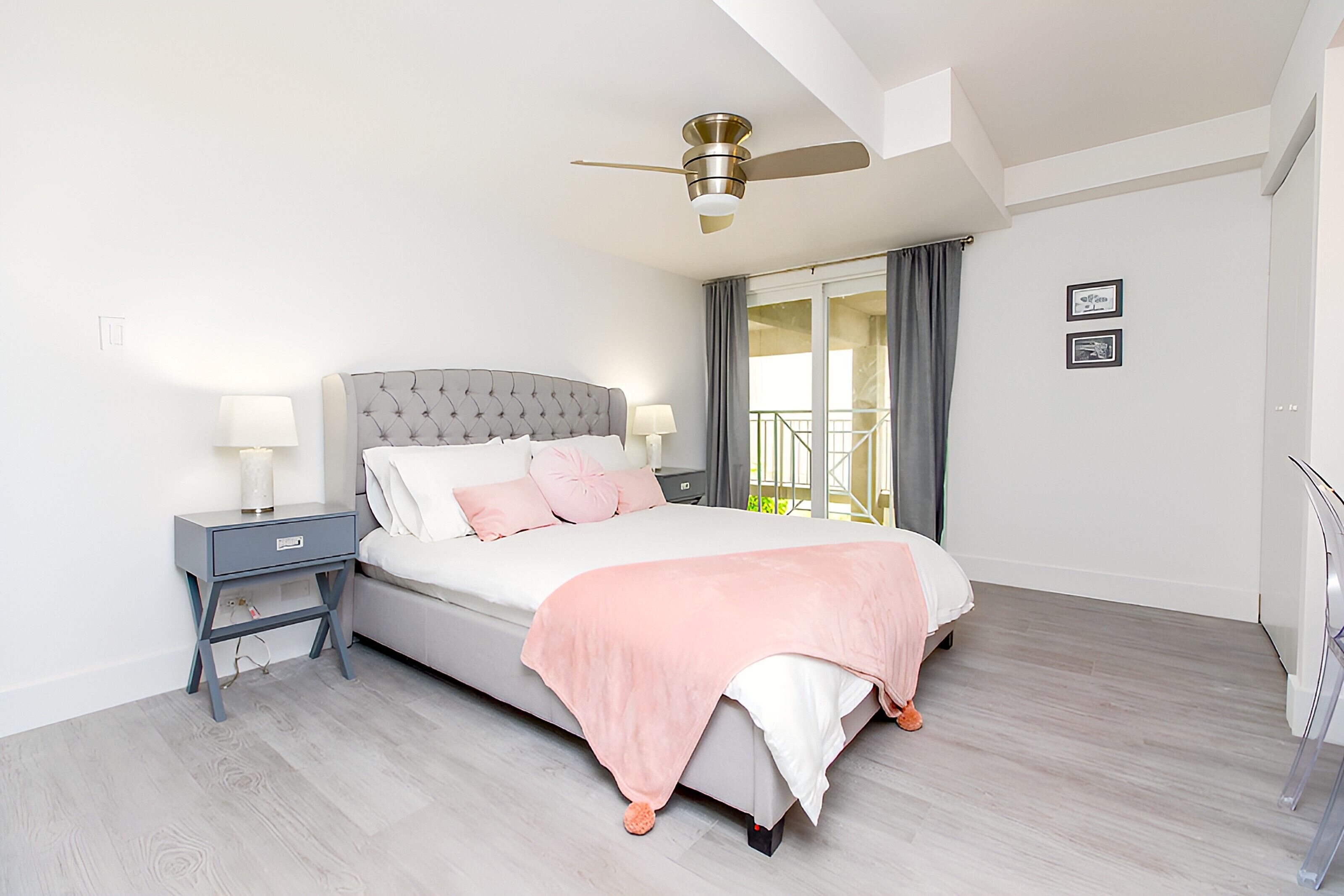 Ein Schlafzimmer mit einem Bett, Nachttischen, einem Deckenventilator und einem Balkon mit Vorhängen.