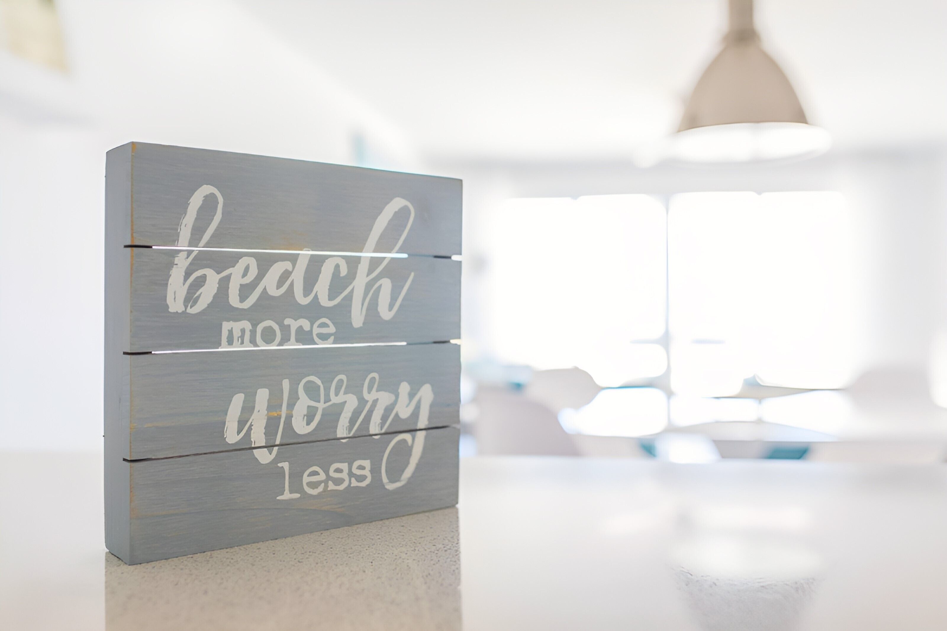 A wooden sign with the text "beach more worry less" on a countertop.