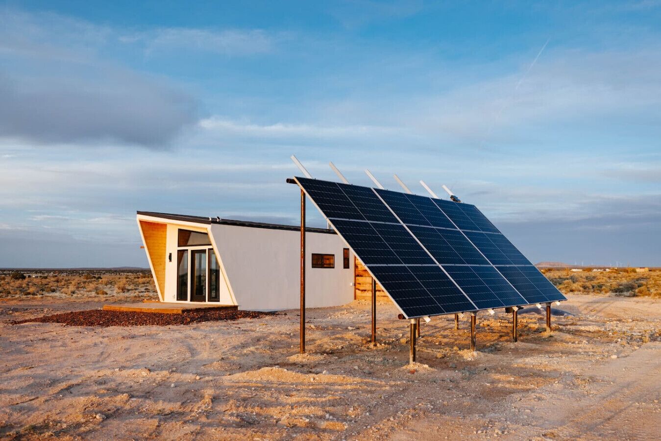 Une maison moderne et minimaliste, dotée d’un ensemble de panneaux solaires, située dans un paysage désertique.