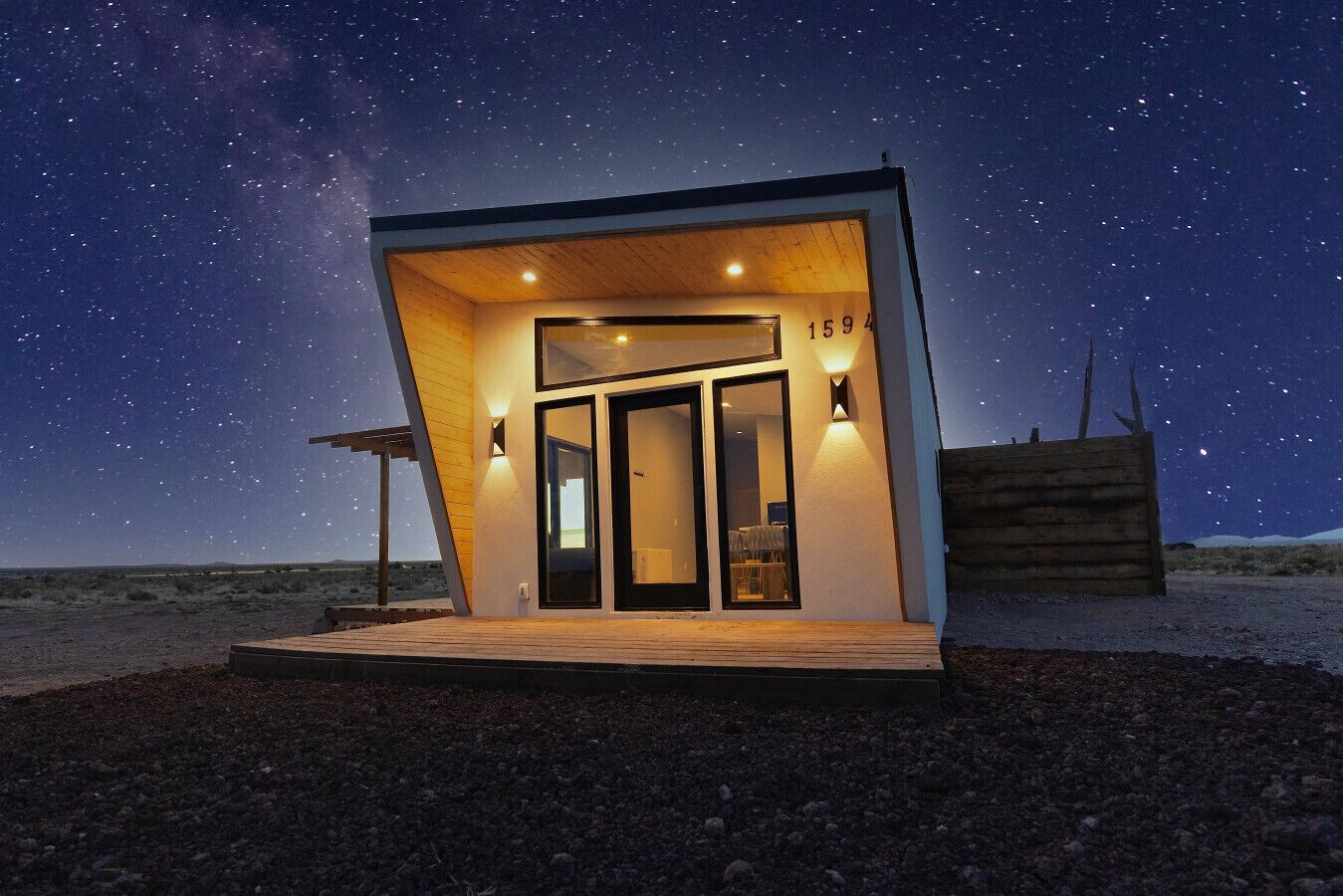 Un bâtiment moderne, de plain-pied, doté d’une terrasse en bois, de grandes portes vitrées et offrant une vue sur un ciel étoilé.
