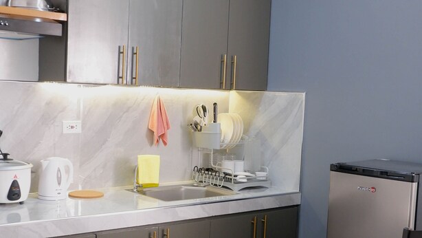 A modern kitchen with grey cabinets, a stainless steel refrigerator, and a dining area with a table and chairs. - CJ Apartments (Olongapo)