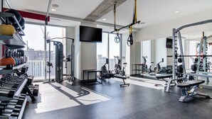 A modern gym with various exercise equipment, large windows, and a city view.