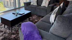 A modern living room with a gray sofa, a coffee table, and a view of a cityscape through large windows.