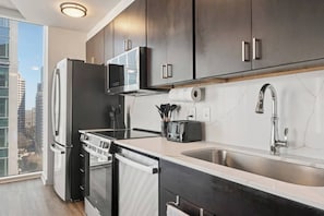 A modern kitchen with dark cabinets, stainless steel appliances, a large window, and a city view.