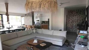 Un salon moderne avec un grand canapé en forme de L, une table basse ronde et un luminaire suspendu en rotin.