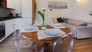 A dining area with a round table set for four, clear chairs, a white cabinet, a microwave, and a sofa in the background. - Apartments Florence I Portici (Firenze)