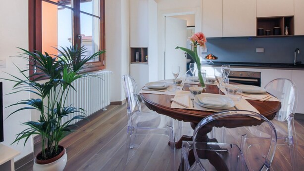 A dining area with a wooden table and clear chairs, a potted plant, and a view of the outside. - Apartments Florence I Portici (Firenze)