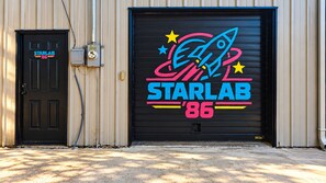 A garage door with a colorful StarLab '86 logo, a black door with a StarLab sign, and a utility box to the left. - StarLab '86 -Downtown Pet Friendly (Fort Smith)