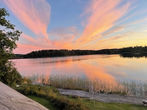 A calm lake at sunset with a wooden dock and dense forest in the background.