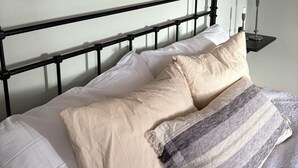 A bed with a black metal headboard, beige and white pillows, and a striped blanket. Two framed paintings hang above the bed.