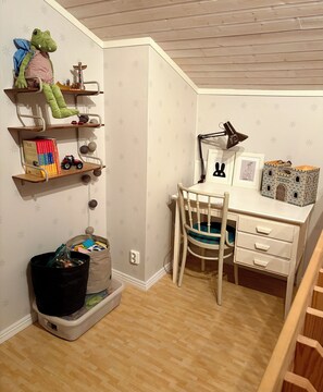 A child's room with a desk, chair, shelves with toys, and books.