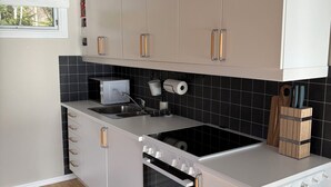 A modern kitchen with white cabinets, a black tiled backsplash, a built-in oven, and a window with a view of trees.