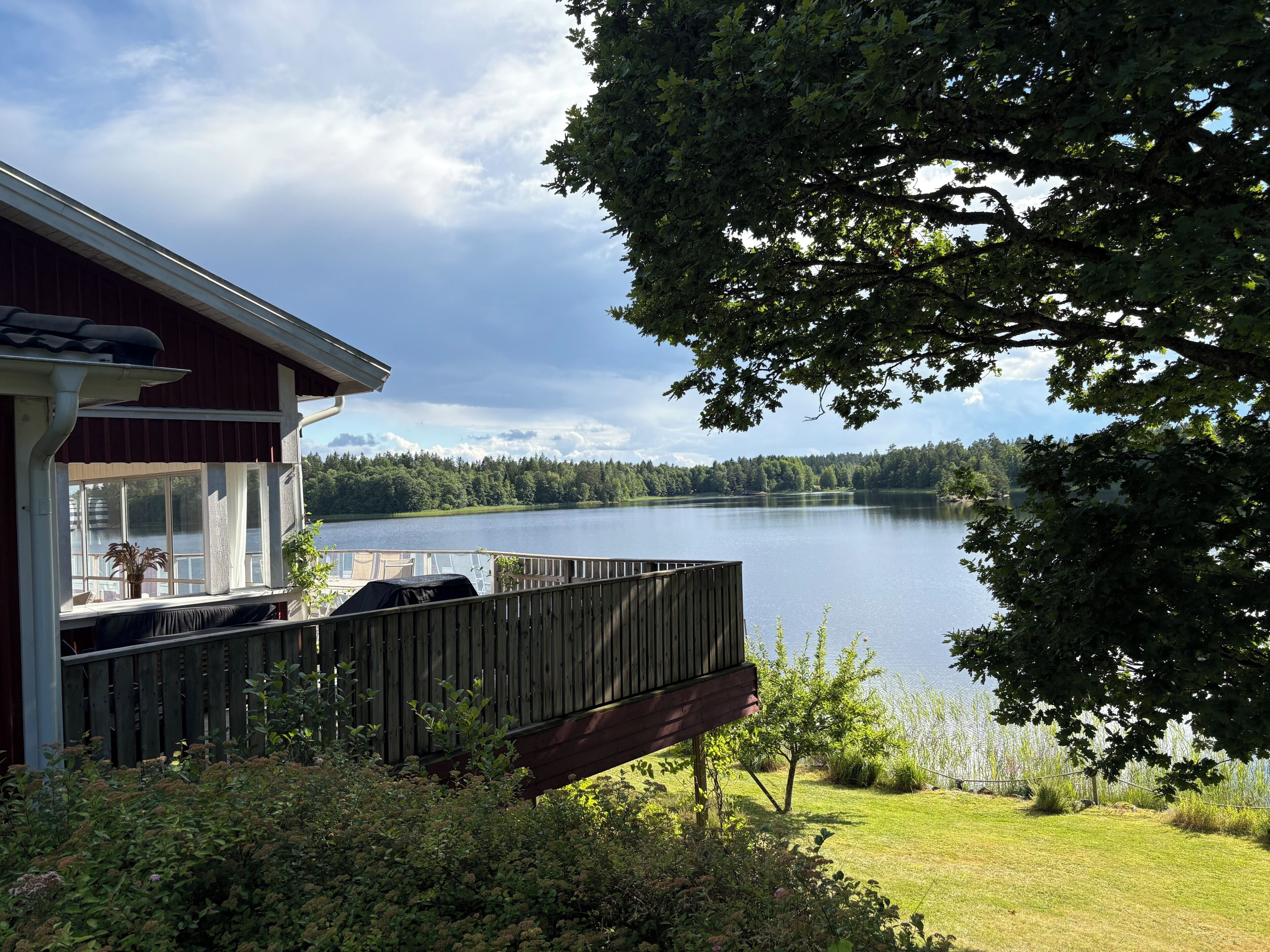 A lakeside property with a deck, a covered outdoor seating area, and a view of the lake and forested landscape.